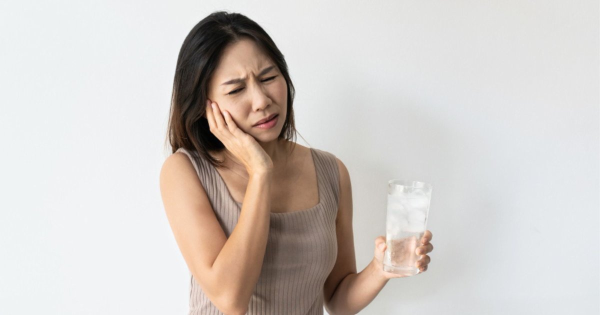 Person experiencing tooth sensitivity while drinking a cold beverage in North Lakes